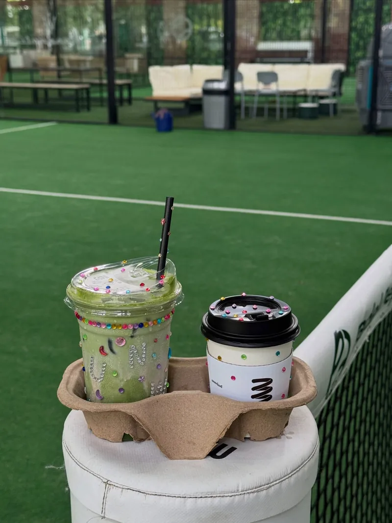 A matcha drink and a coffee from unwind.kl beside a padel court
